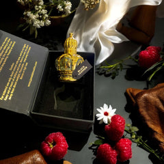 Black Leather Oud perfume oil in an ornate bottle packaging, surrounded by raspberries and floral accents.