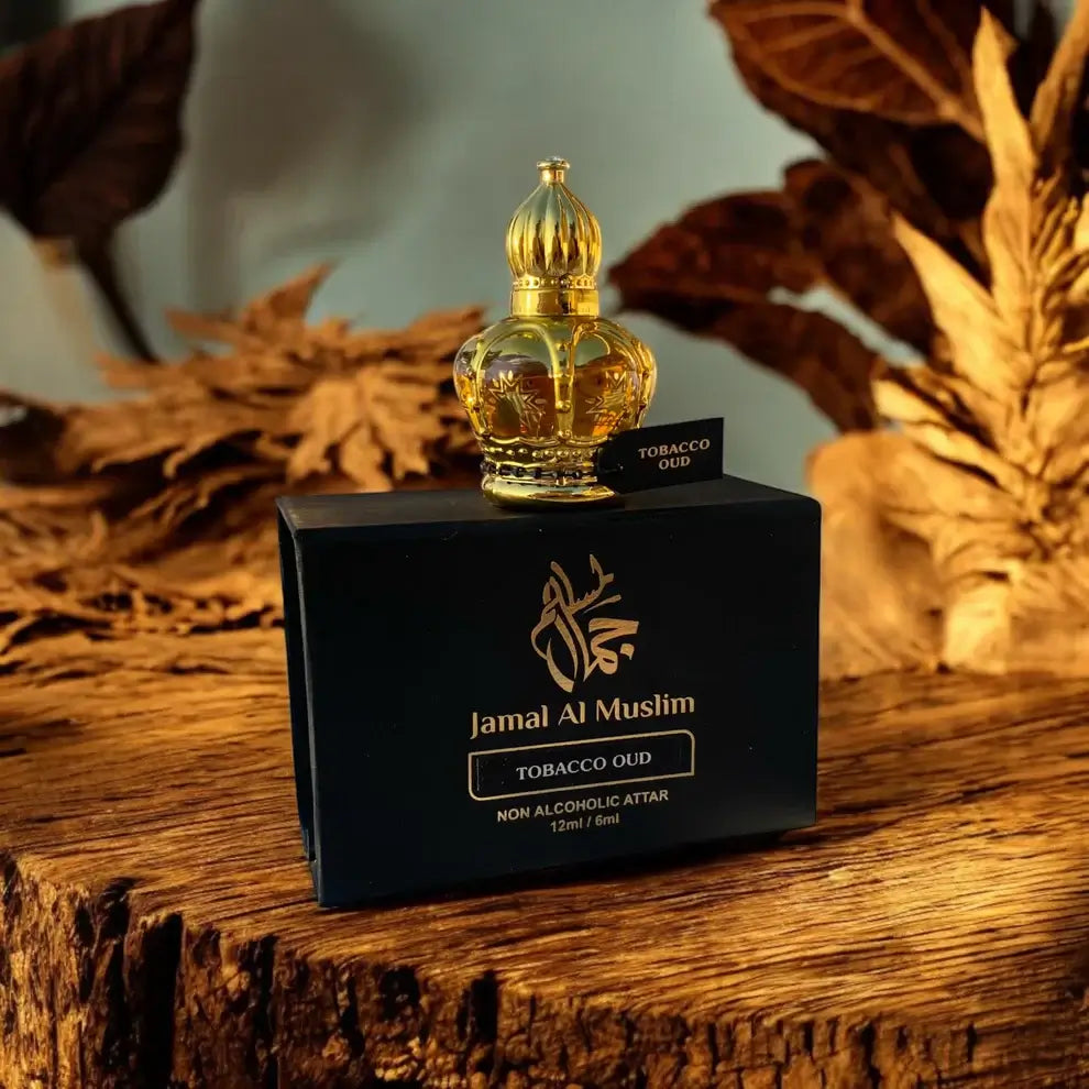Tobacco Oud attar bottle, 12ml, by Jamal Al Muslim, displayed on a wooden surface with foliage in the background.